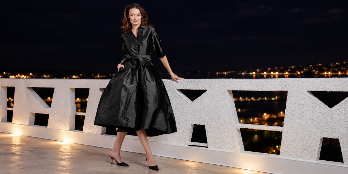 Model wearing a black silk belted dress from Lizzie P.M. on a terrace at night